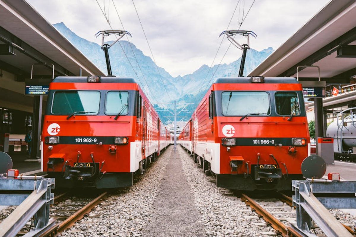 Two red electric trains standing side by side at a railway station.